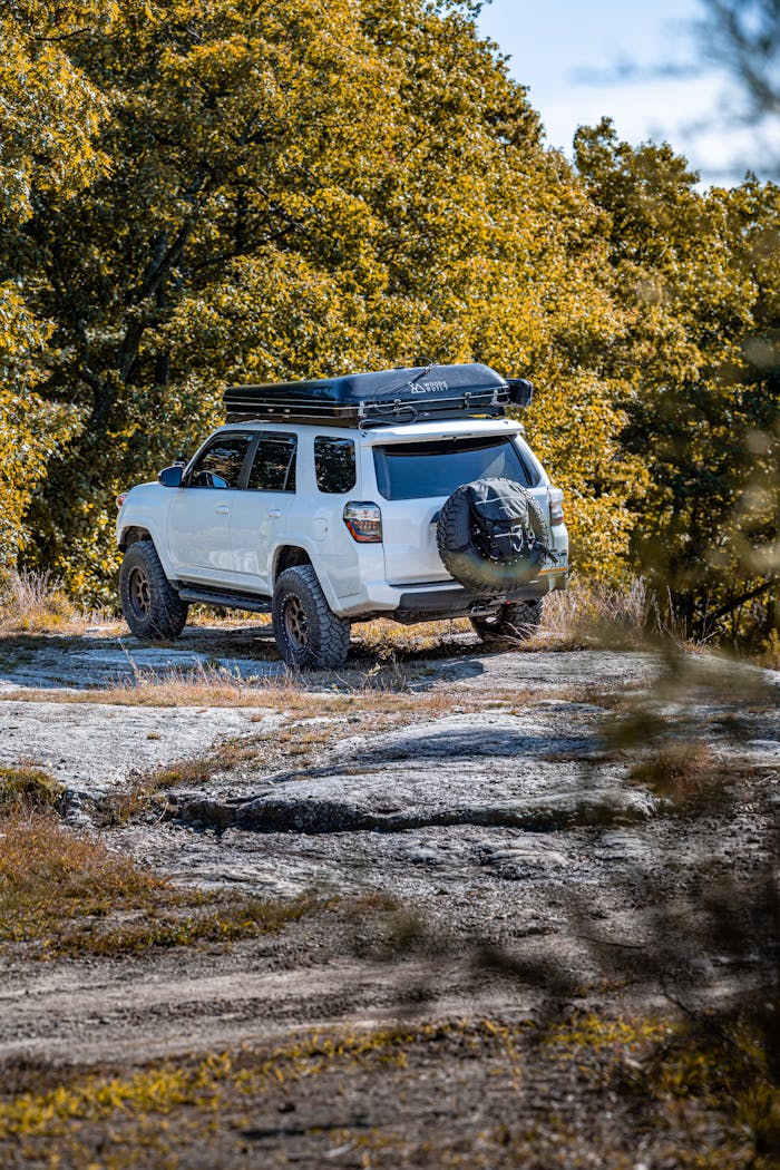 White SUV parked on a rocky terrain in a forested area, showcasing outdoor adventure.